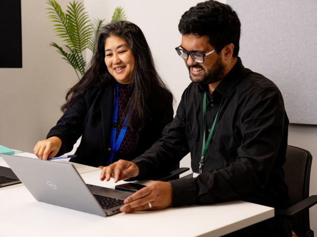 Two members of smiling and looking at a screen together
