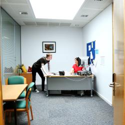 A woman sits at a deskin an office, and a man stands next to her. They appear to be talking. 