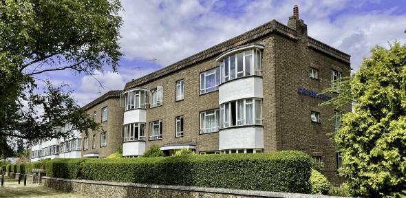 Causewayside An image of a three-story brick building with white windows, behind a short wall and hedge.