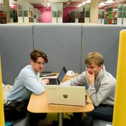 Two students in a library looking at a laptop