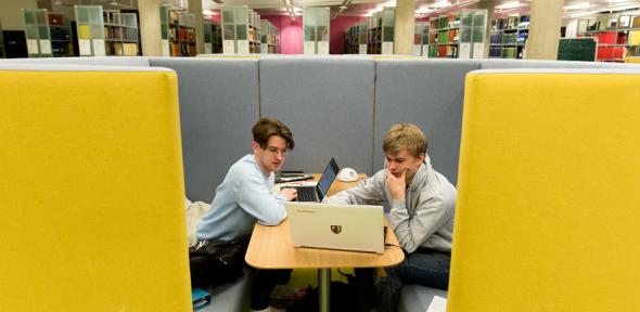 Two students in a library looking at a laptop